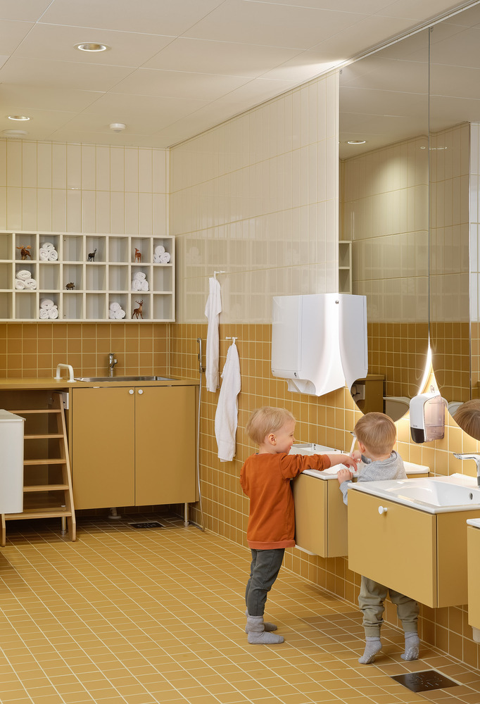 Bathroom with mustard-yellow tile walls, floating vanity, and two children at the sinks