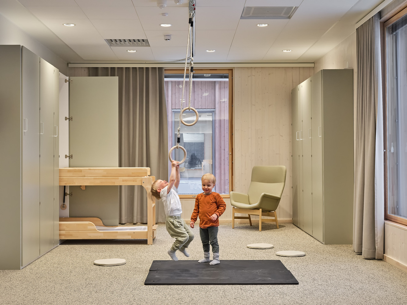 Playroom with bunk bed, suspended gymnastics rings, and two children on a terrazzo floor