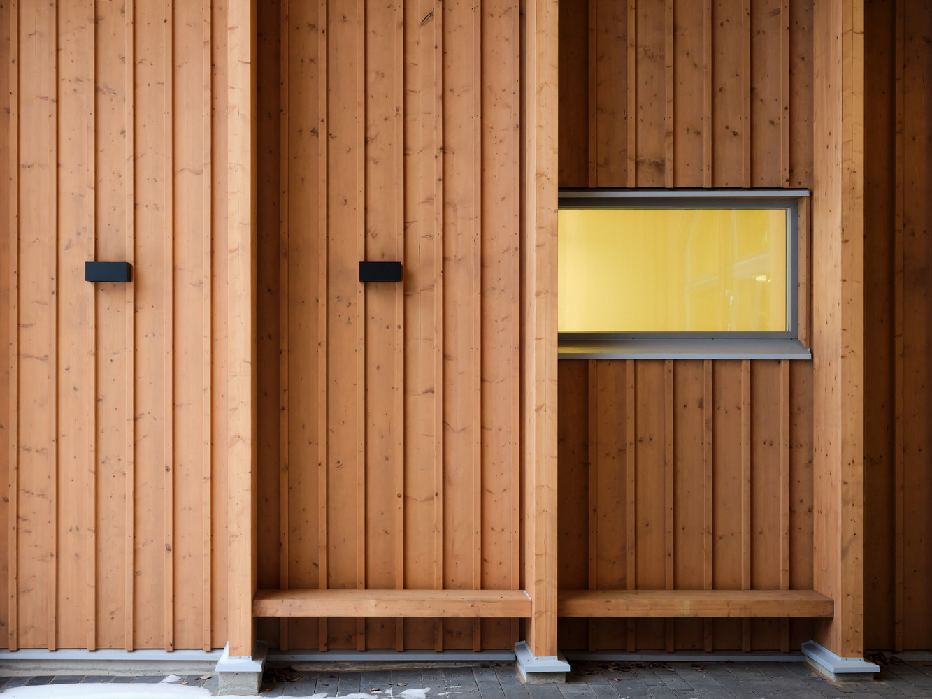 Timber wall with two built-in benches, black metal fixtures, and a horizontal window with yellow curtain
