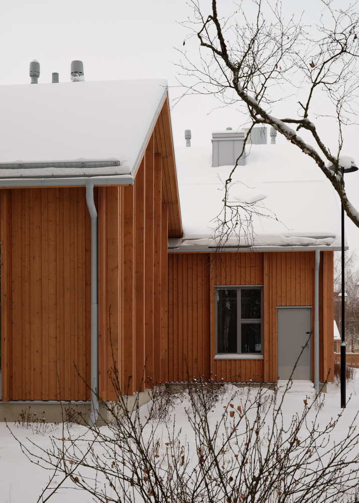 Clustered timber volumes with snow-covered pitched roofs and a bare tree in the foreground