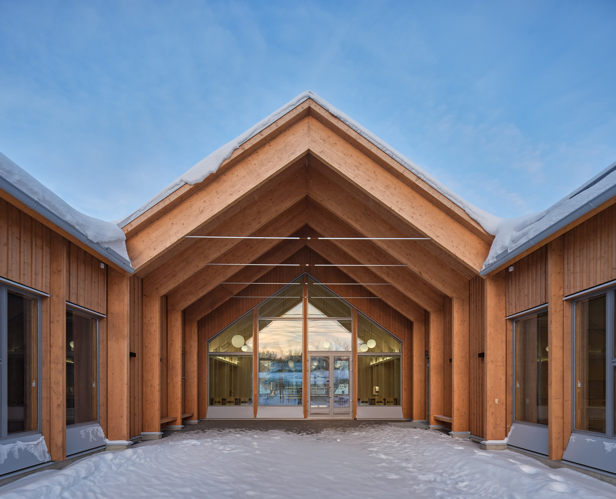 Covered courtyard entry framed by laminated timber arches leading to glazed doors in winter light