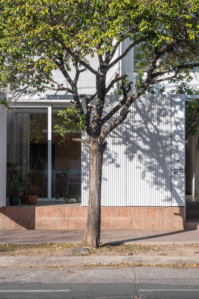 Corrugated metal facade and brick base partially shaded by a mature tree in the foreground