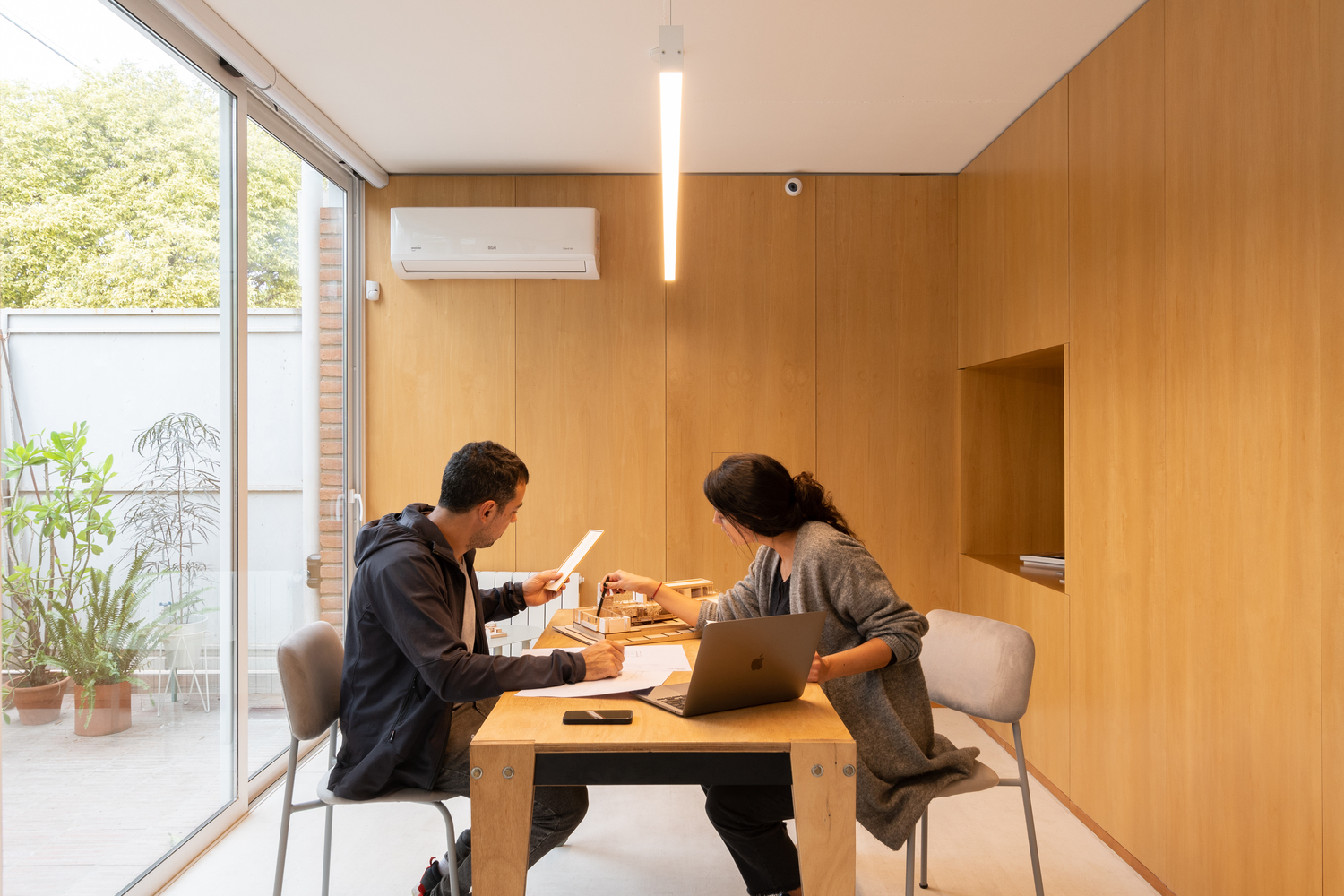 Two people working at a timber table surrounded by plywood wall panels and clerestory glazing