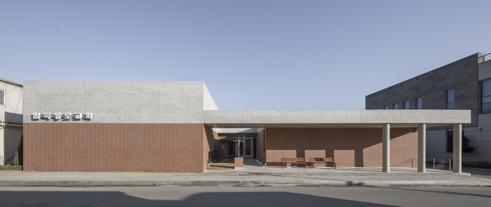 Street view of the low-slung facade combining red brick volumes with a white concrete canopy