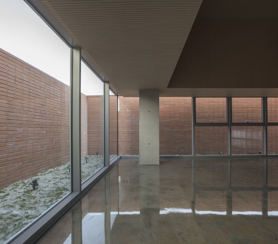 Covered interior space with concrete column and floor-to-ceiling glass overlooking a planted courtyard