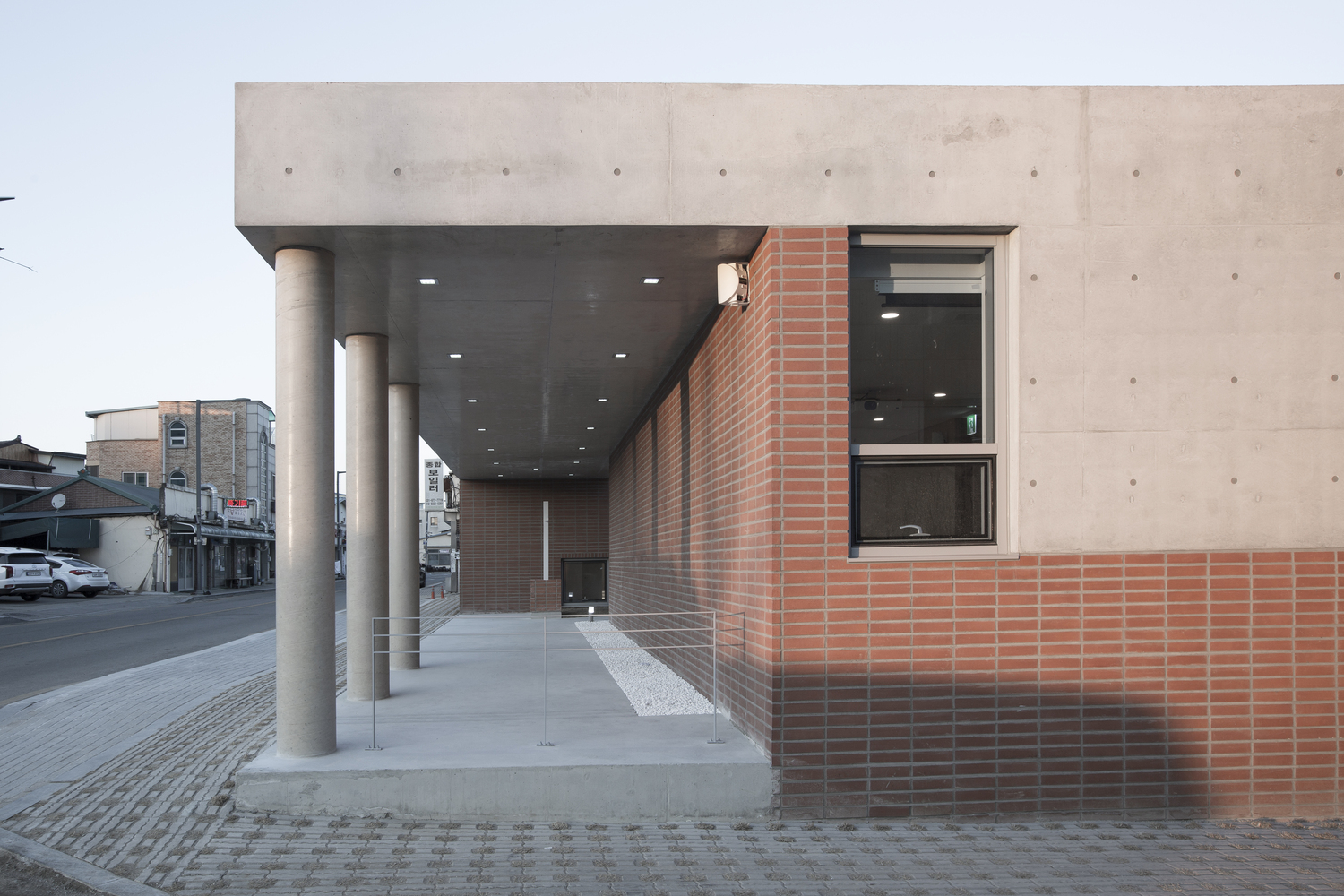 Covered entrance portico with cylindrical concrete columns and red brick facade at dusk