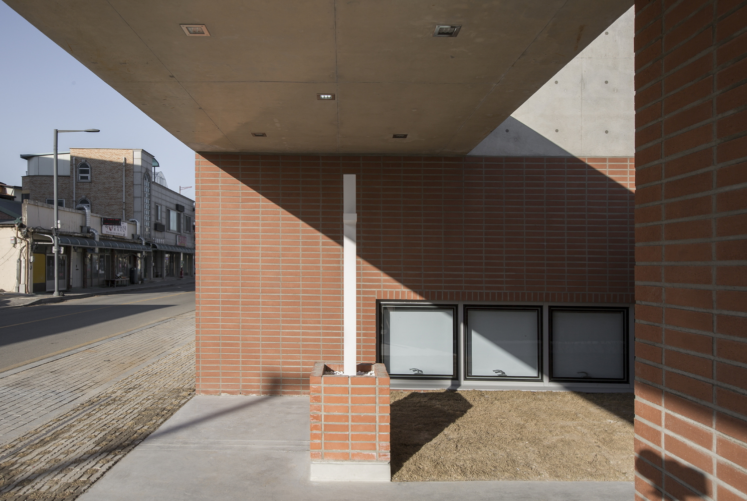 View under the cantilevered concrete soffit showing brick walls and planted bed in shadow