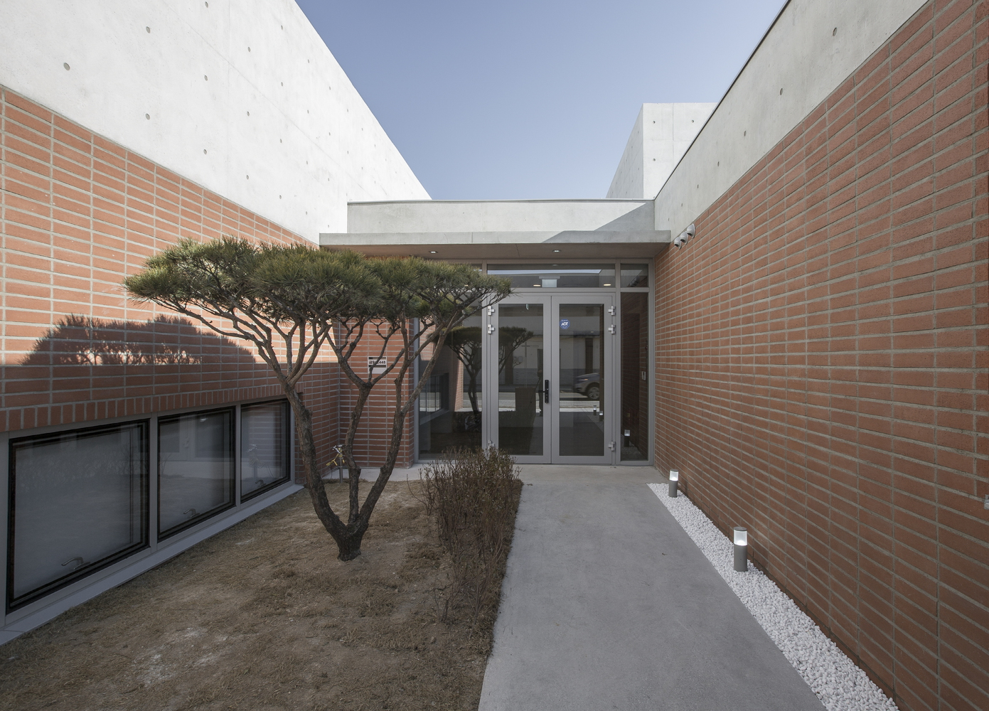Courtyard passageway between red brick walls with pruned tree and gravel border under open sky