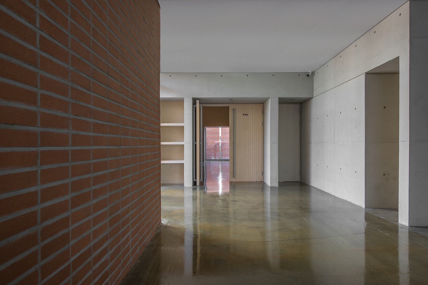 Interior hallway with polished concrete floor reflecting light from distant doorway and exposed brick wall