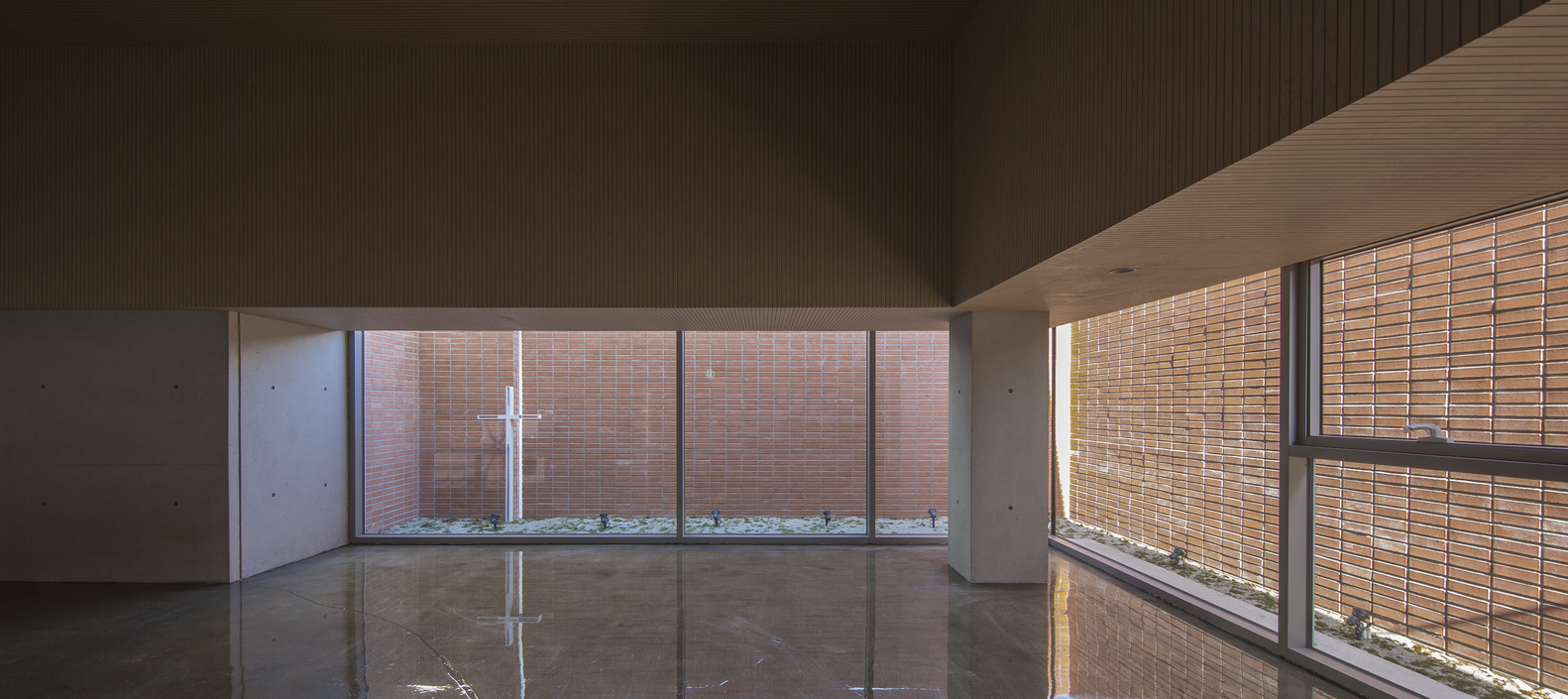 Gallery space with reflective floor and floor-to-ceiling windows overlooking the brick courtyard at sunset