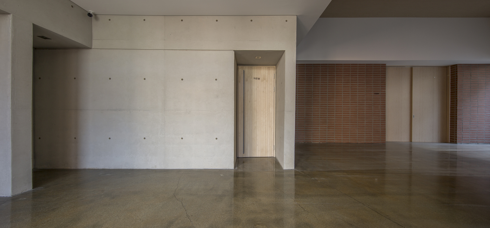 Interior corridor with board-formed concrete walls and polished concrete floors leading to a timber screen