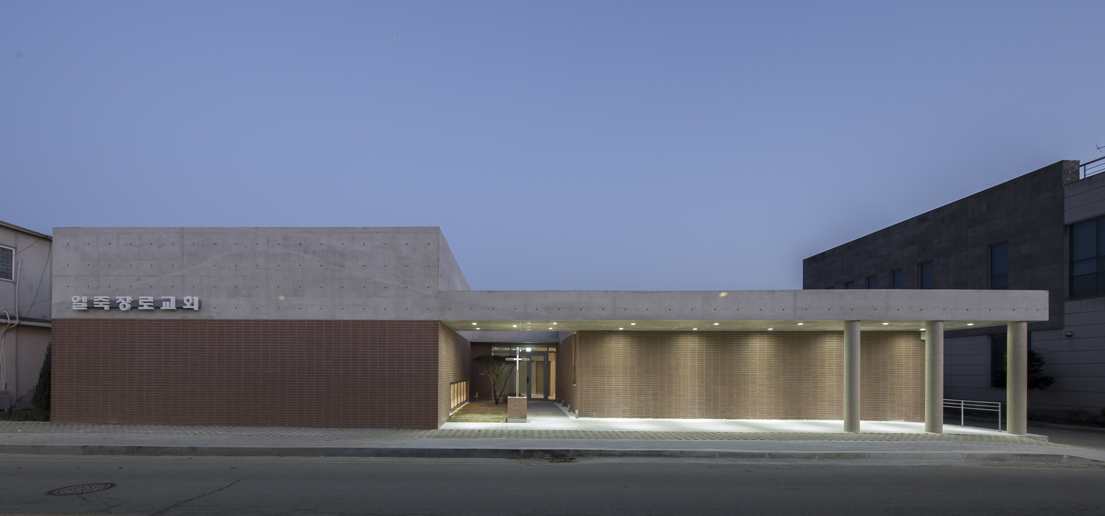 Street facade with concrete volume and terracotta brick screen illuminated at twilight