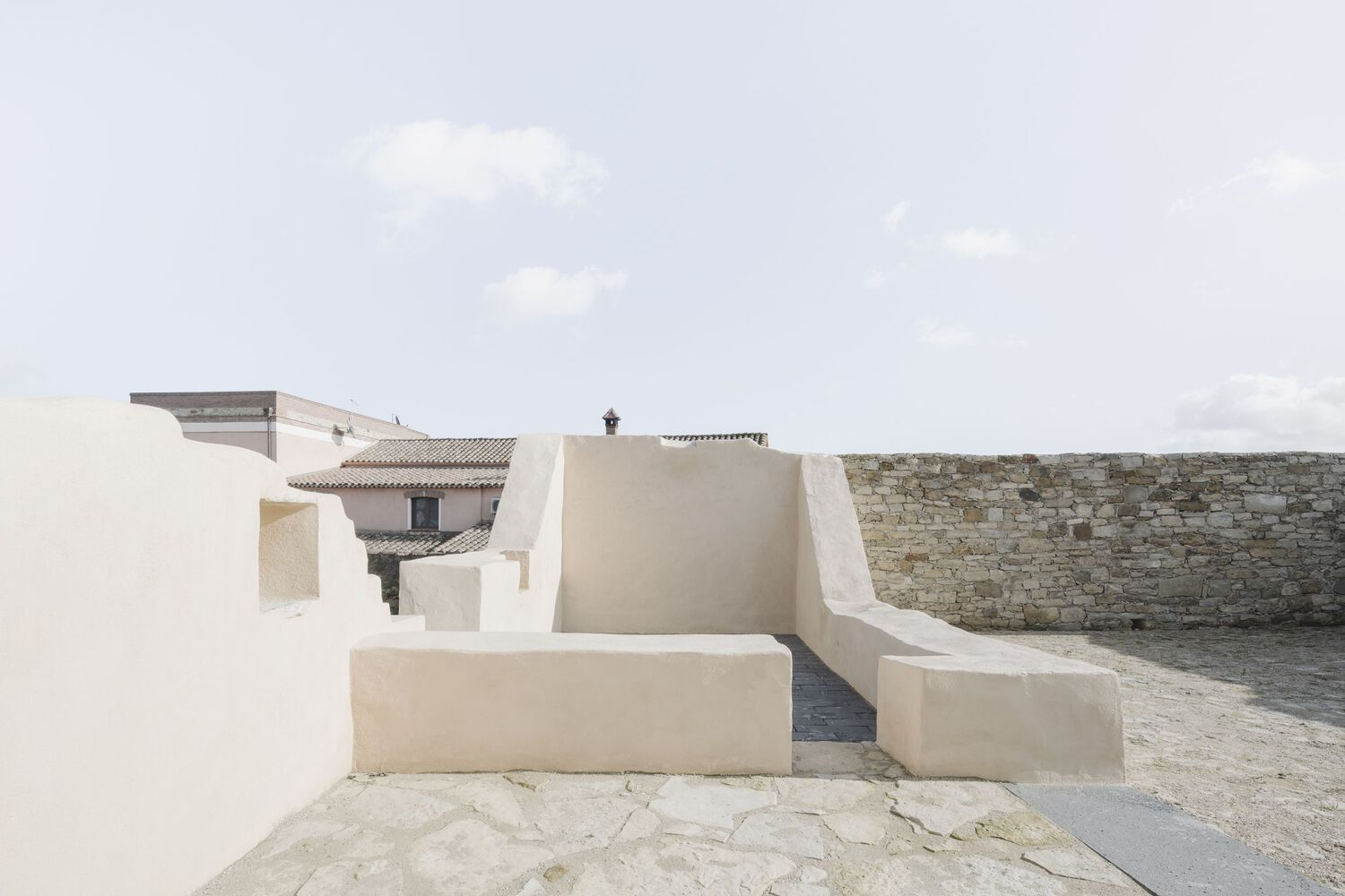Stepped stucco seating form on a stone paved terrace with a church tower visible in the distance