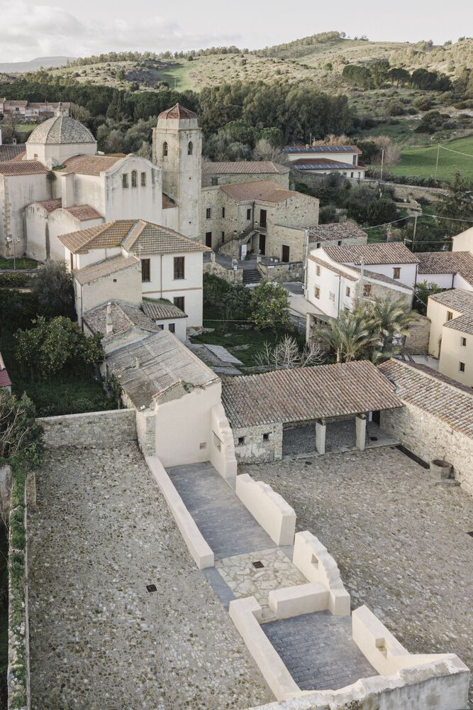 Aerial view of stucco seating platforms in a courtyard surrounded by a hillside village and church tower