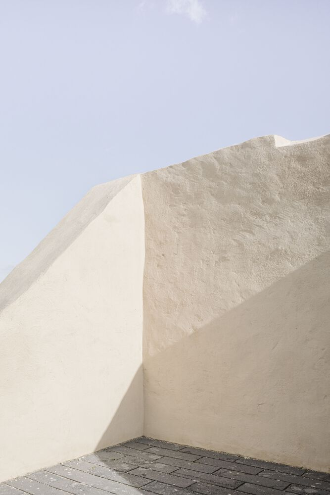 Corner detail of plastered walls meeting at sharp angles above a dark paved floor under pale sky