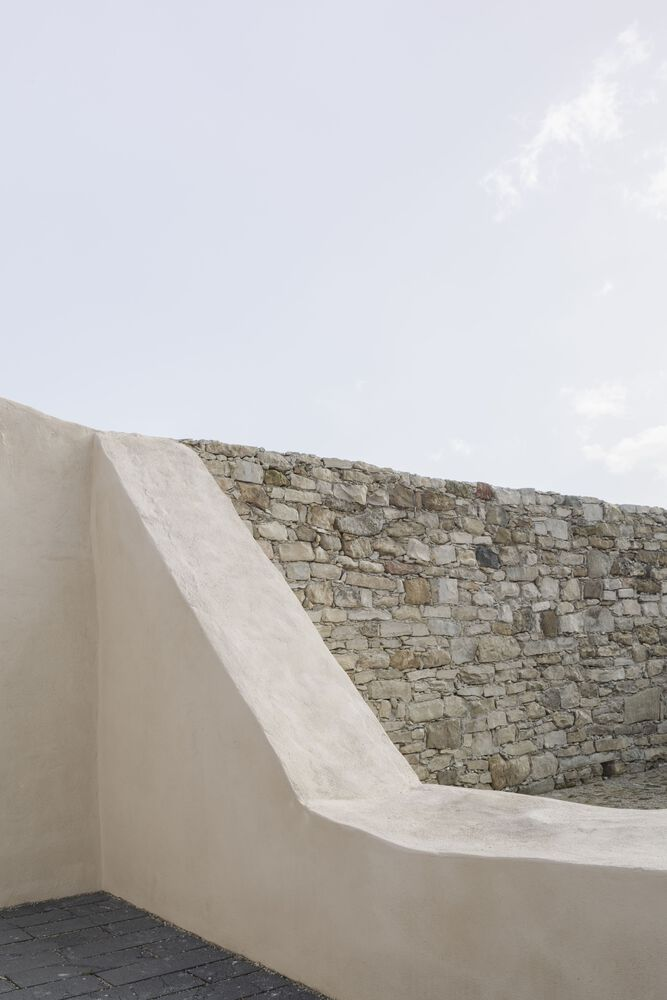Curved plastered parapet wall transitioning into a historic stone wall under cloudy sky