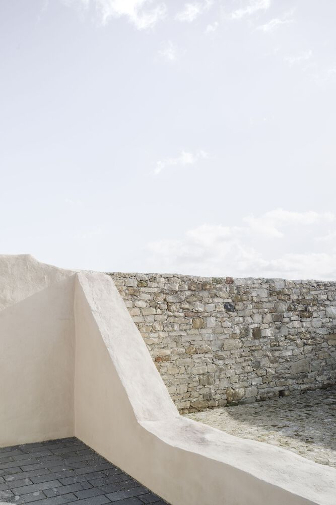 White rendered parapet flowing into an existing stone wall with dark paving below