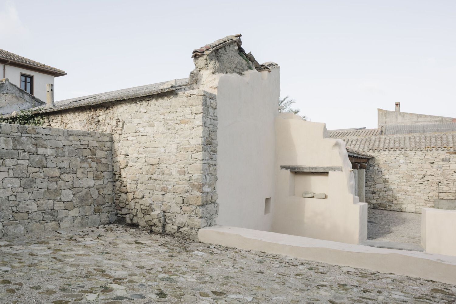 White rendered intervention embedded within deteriorating limestone masonry walls on cobbled paving