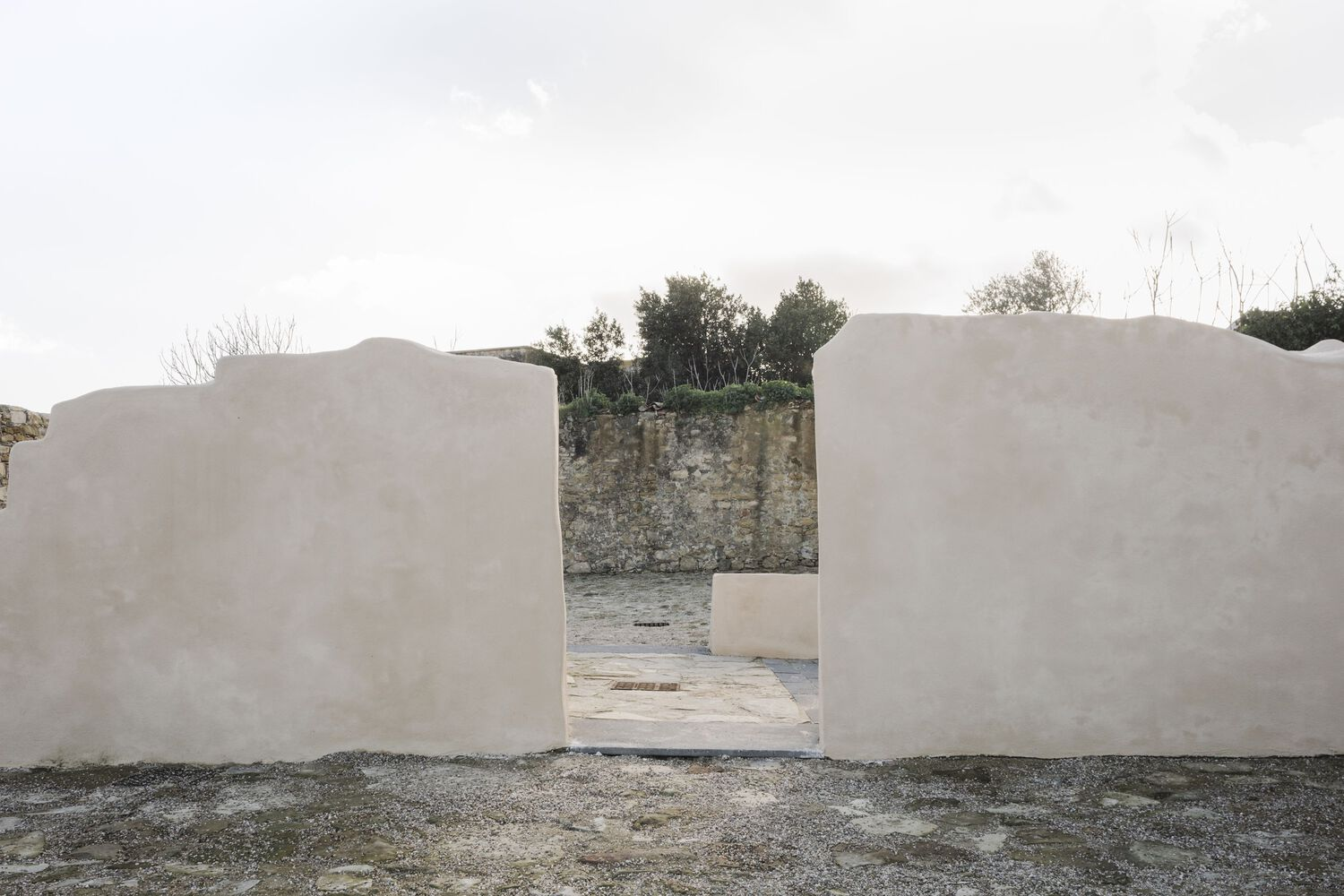 Opening framed by curving white rendered walls revealing stone retaining wall and trees beyond