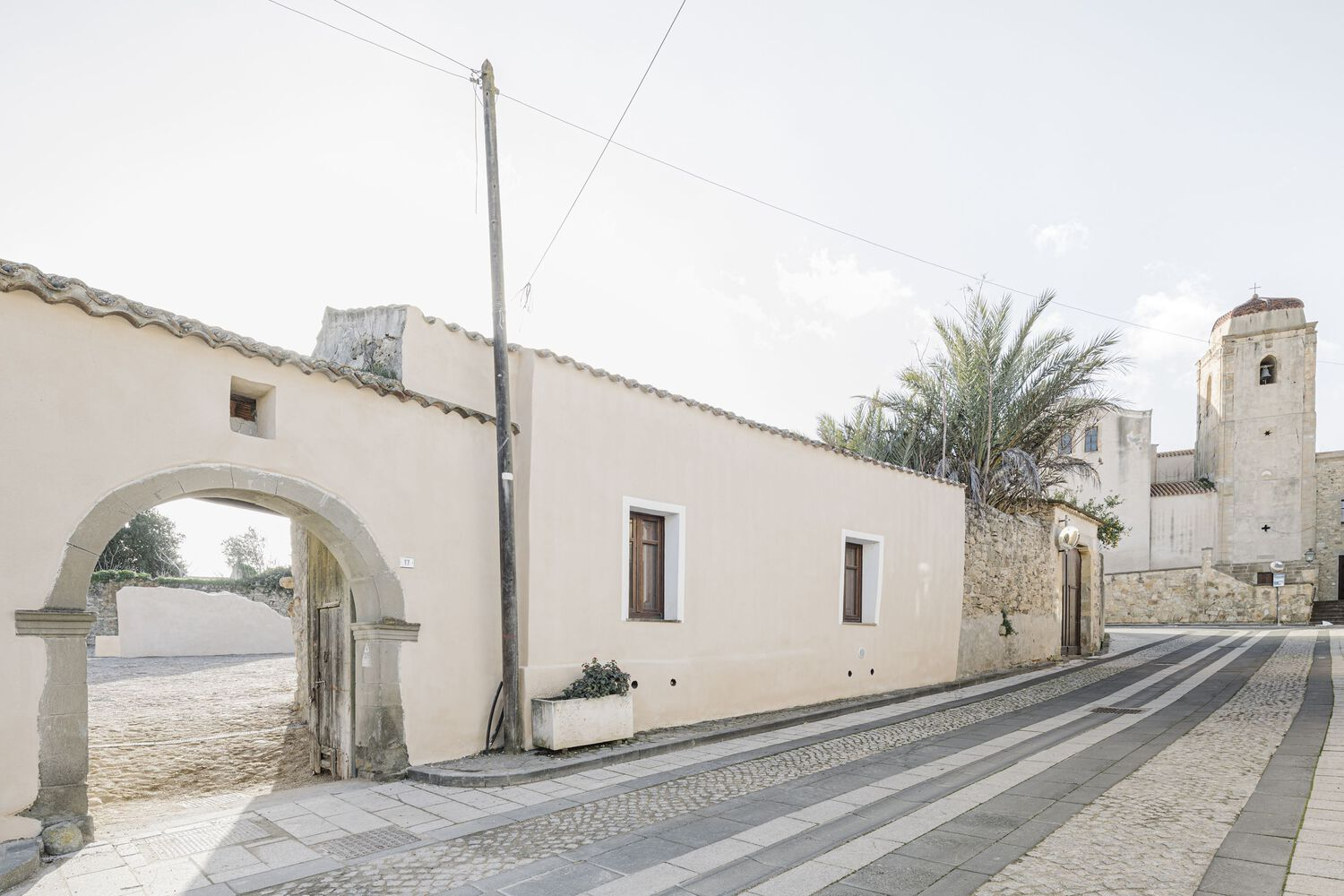 View along a stone-paved street with an arched passageway and a church tower in the distance