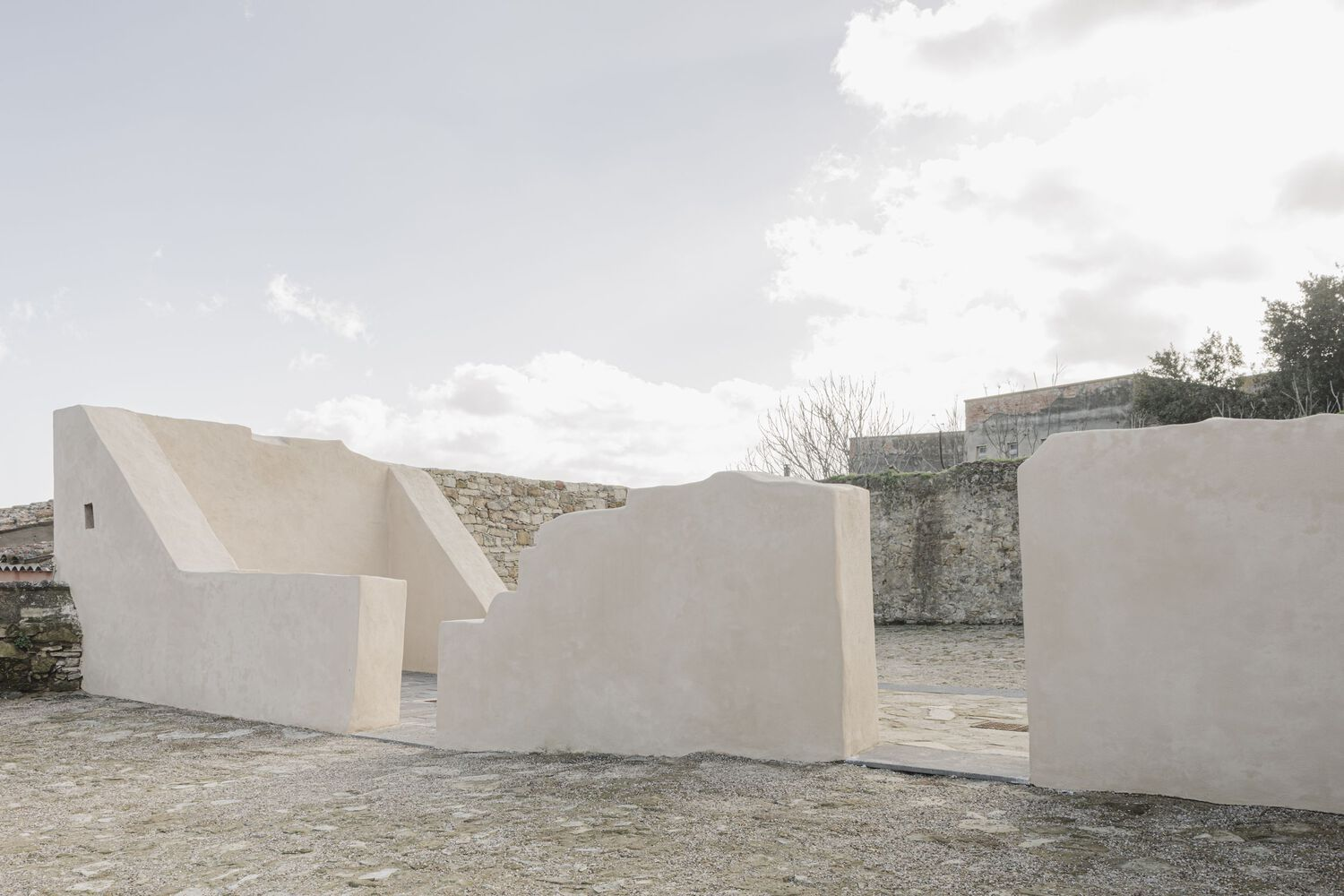 Cluster of white stucco walls with folded rooflines against a cloudy sky