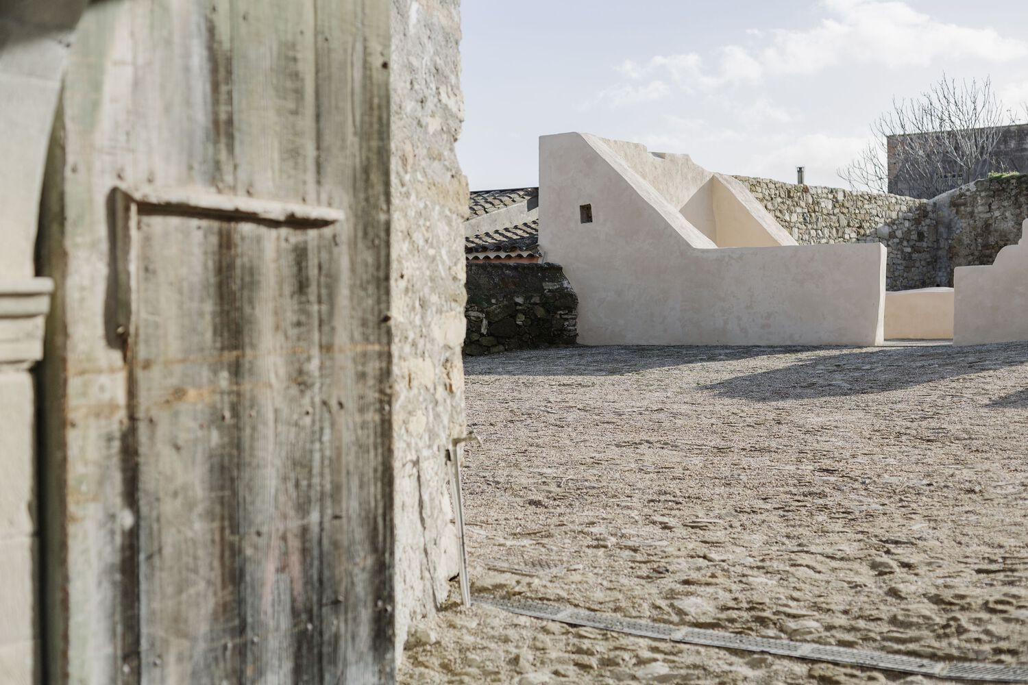 White rendered volumes framed by a weathered timber door and stone pavement in the foreground