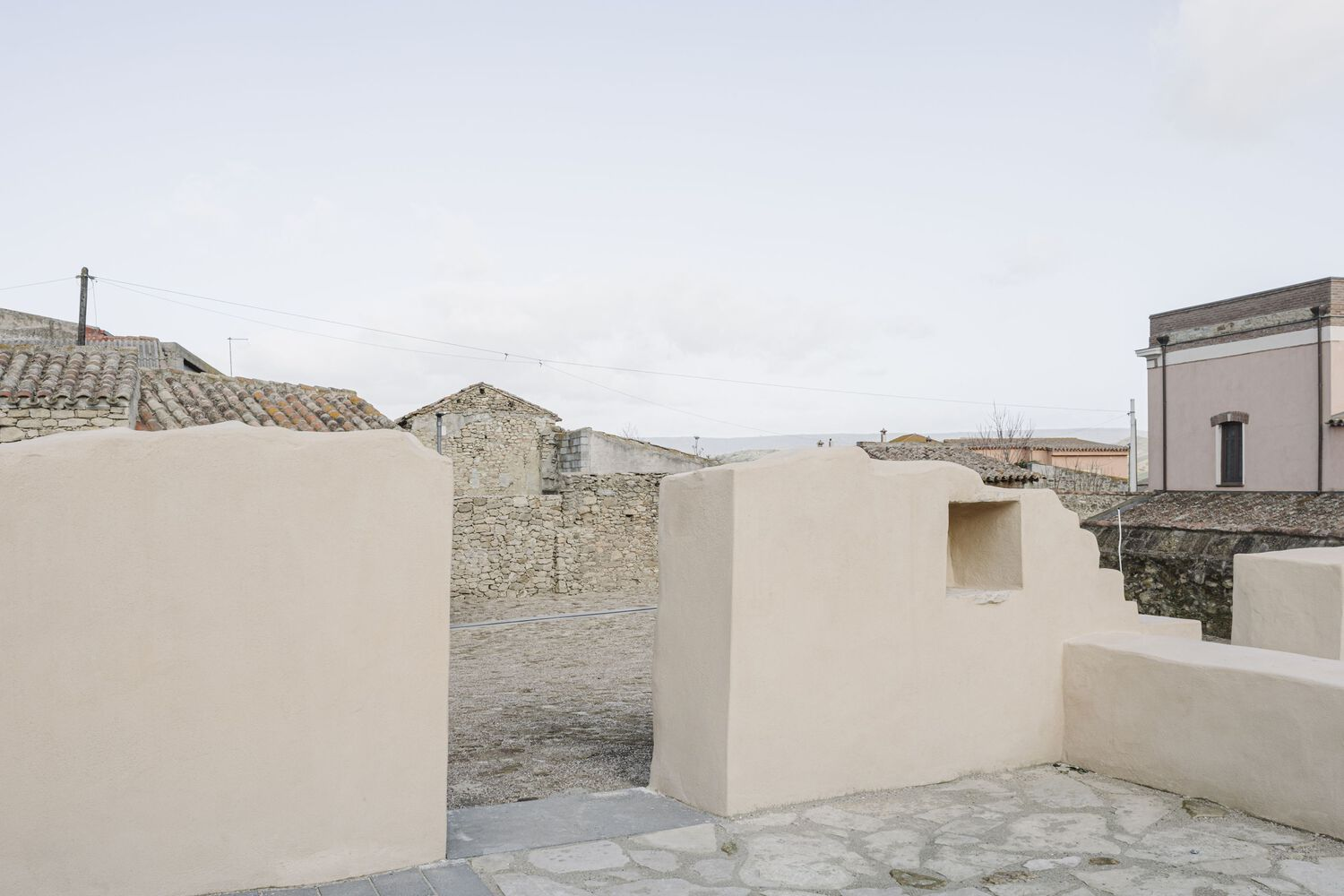 Rooftop terrace with white parapet walls overlooking tile roofs and distant landscape under overcast sky