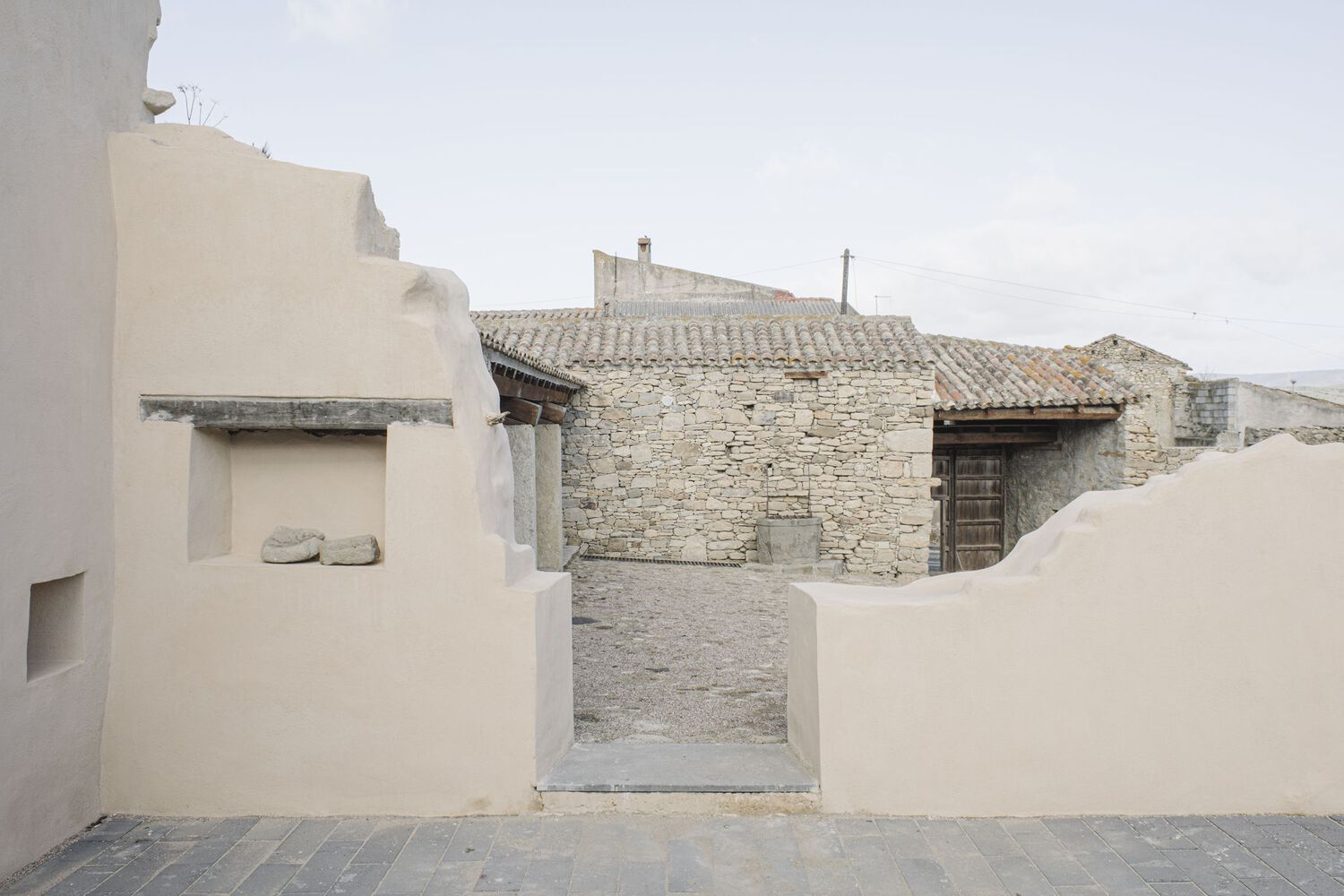 White stucco wall and concrete threshold framing a view toward stone barns with tiled roofs