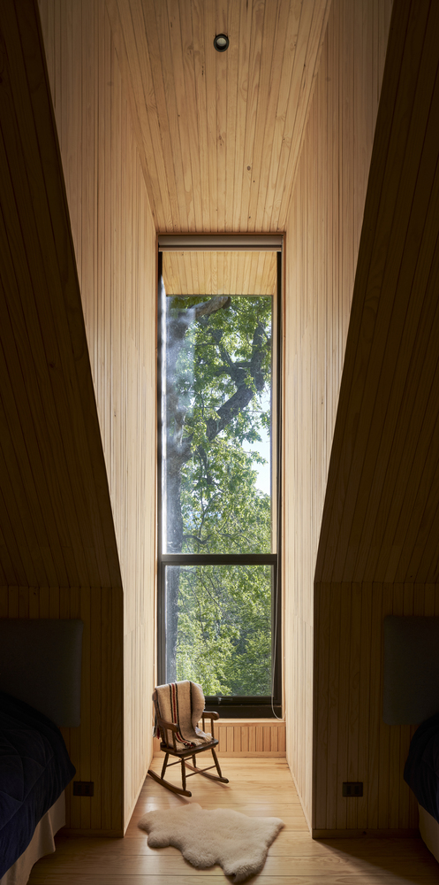 Narrow timber-lined alcove with tall window framing tree views and a rocking chair on the floor