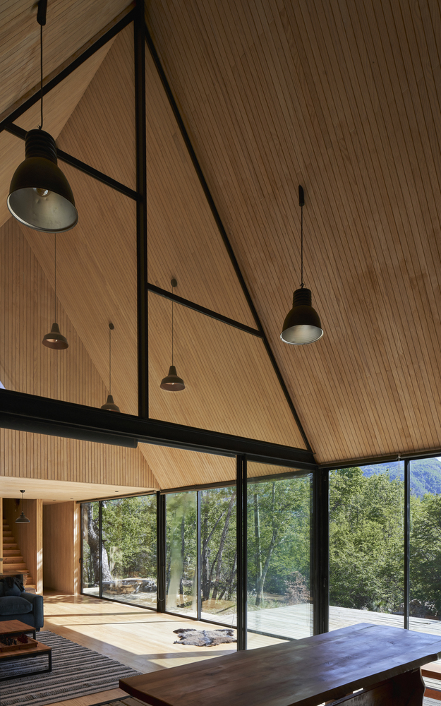 Interior view of the vaulted wood-lined ceiling with black steel beams and pendant lights over the glazed living space