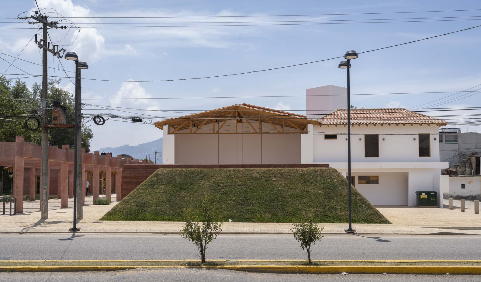 Street view of white stucco volumes with clay tile roofs set behind a sloped grass embankment