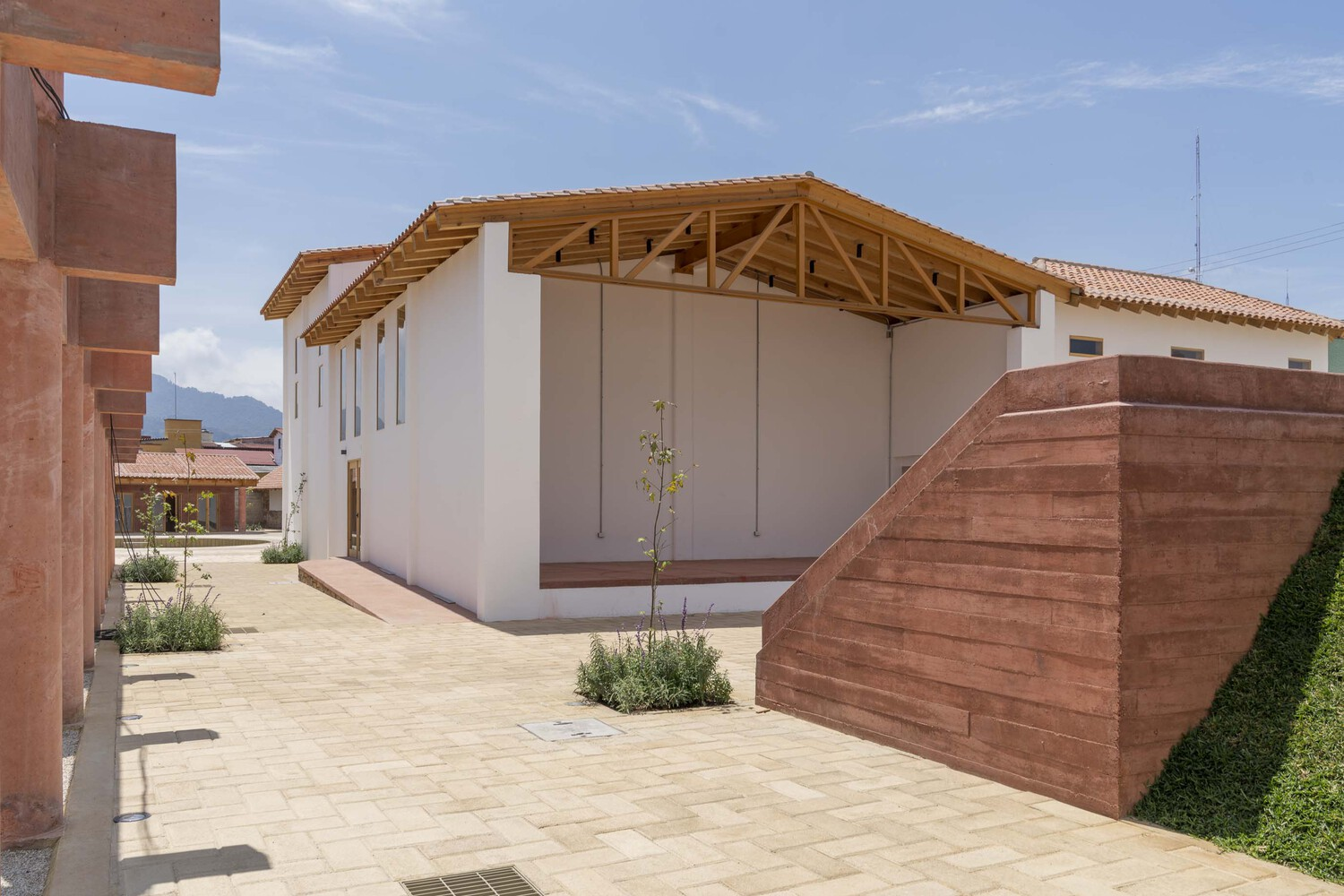 White plastered hall with exposed timber roof trusses beside stone paved courtyard and planted beds