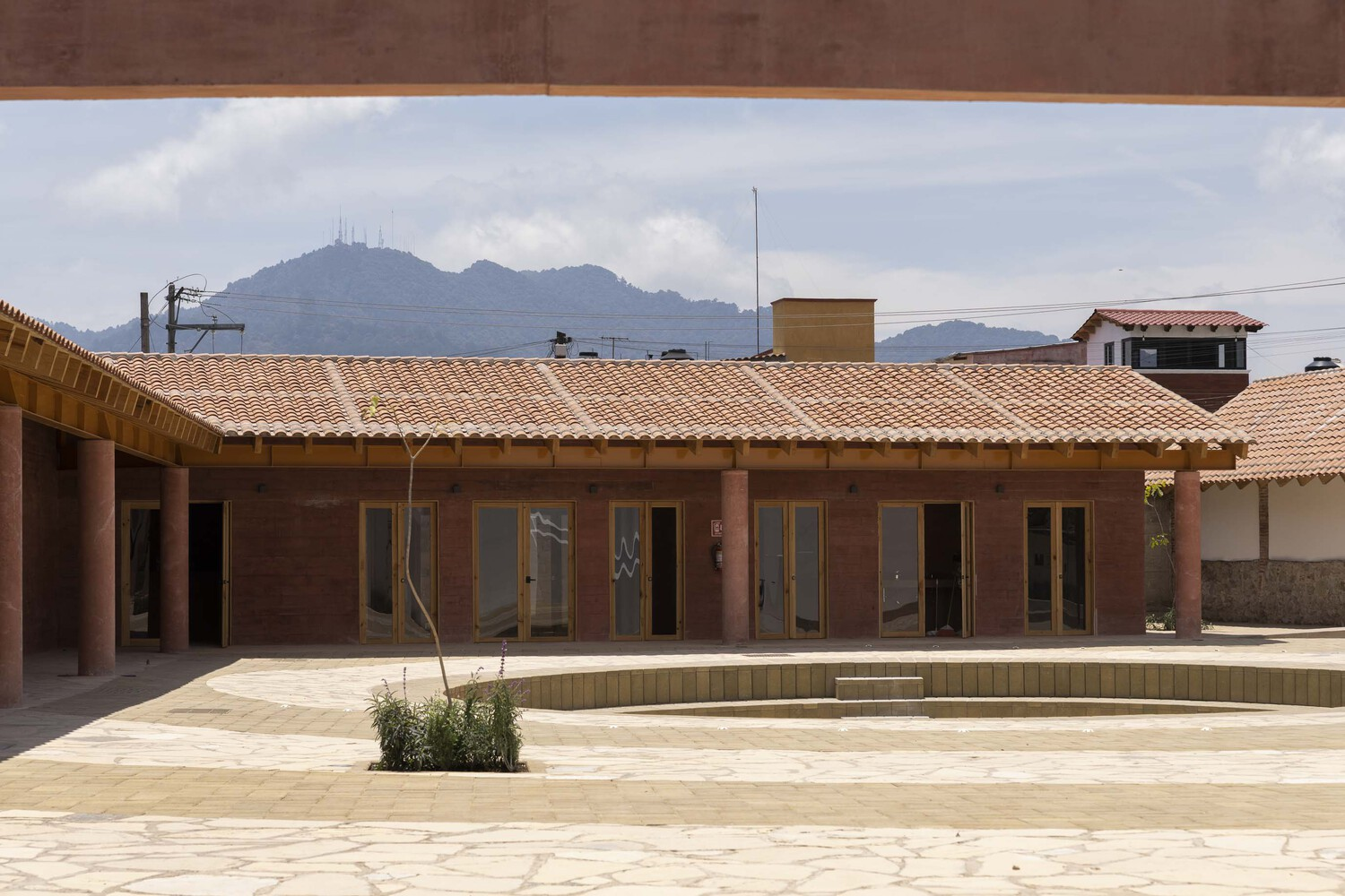 Courtyard facade with rammed earth walls and glazed doors beneath timber trusses and clay tile roof