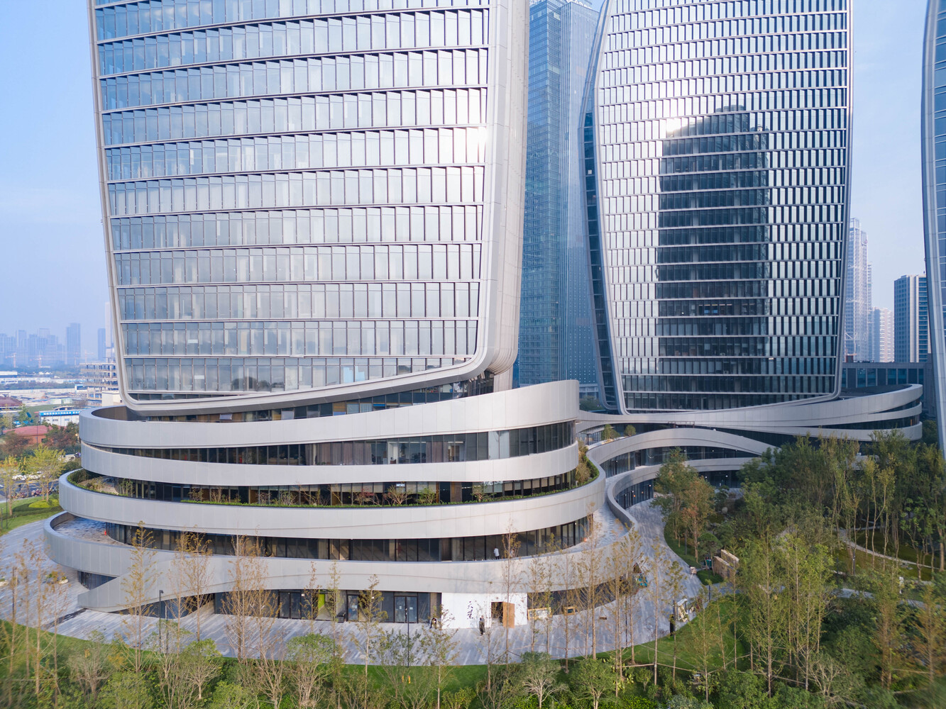 Elevated view of the ribboned podium base wrapping the glass tower bases surrounded by spring trees