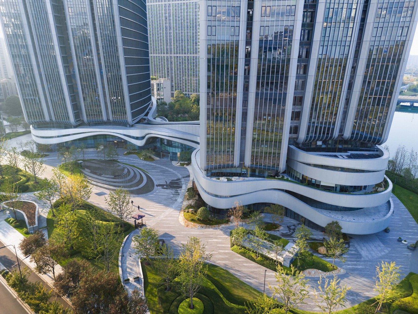 Aerial view of the curving paved plaza with planted beds between the ribbon-clad podium levels
