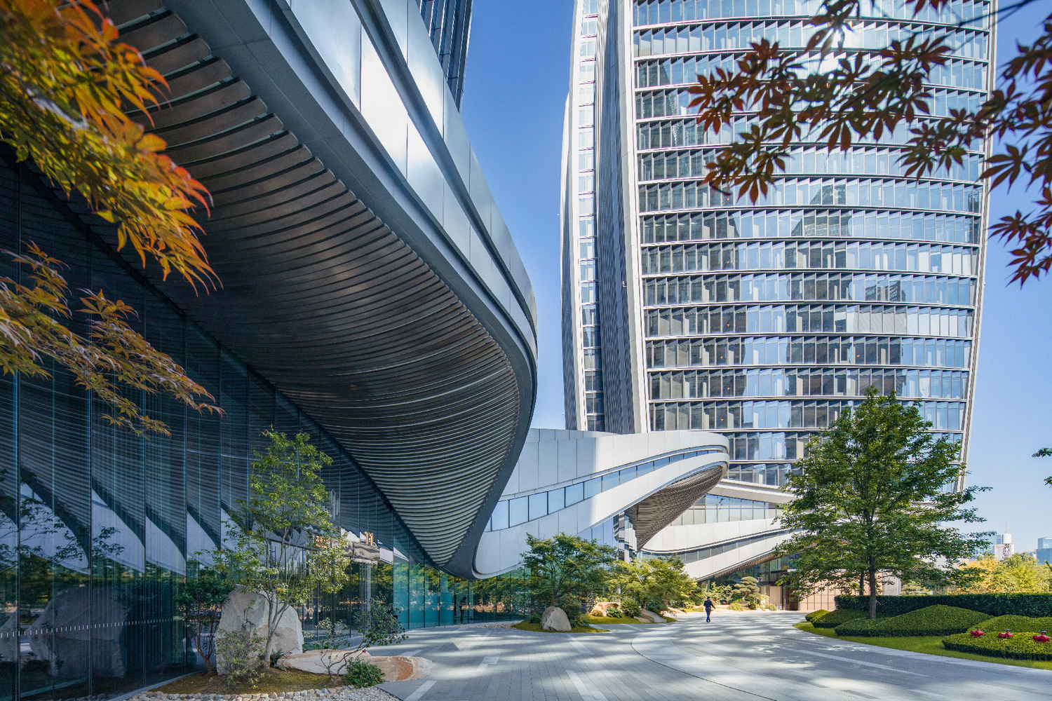 Ground-level view of the glass facade with ribbon louvers framed by autumn foliage overhead