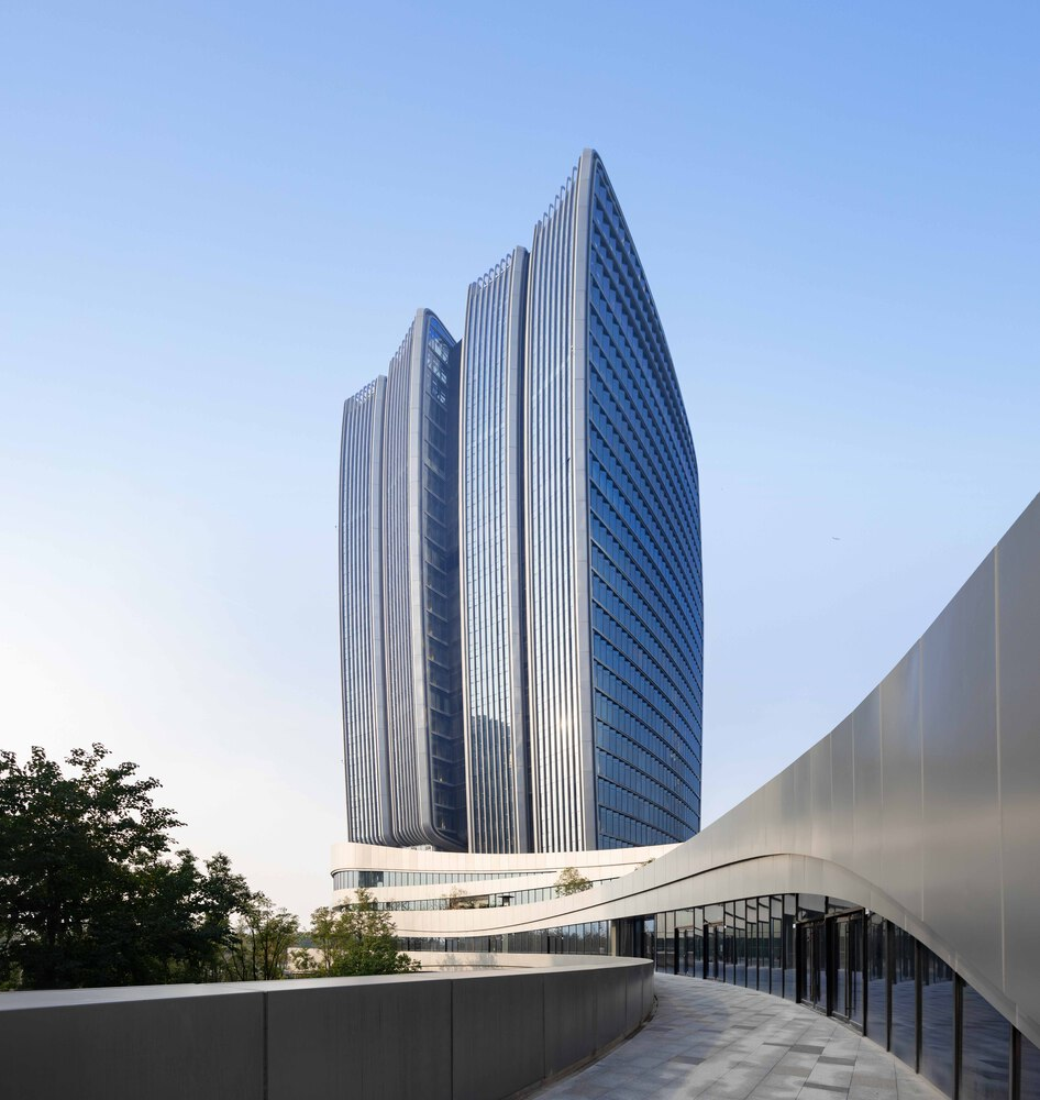 Vertical-ribbed tower facade rising above a curved podium base framed by trees