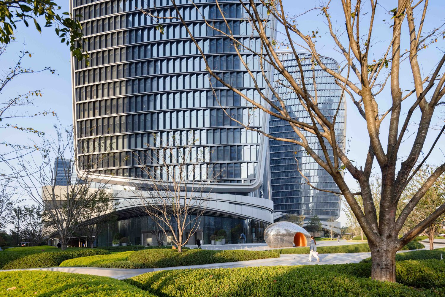 Glass curtain wall towers behind landscaped grounds with hedges and bare winter trees