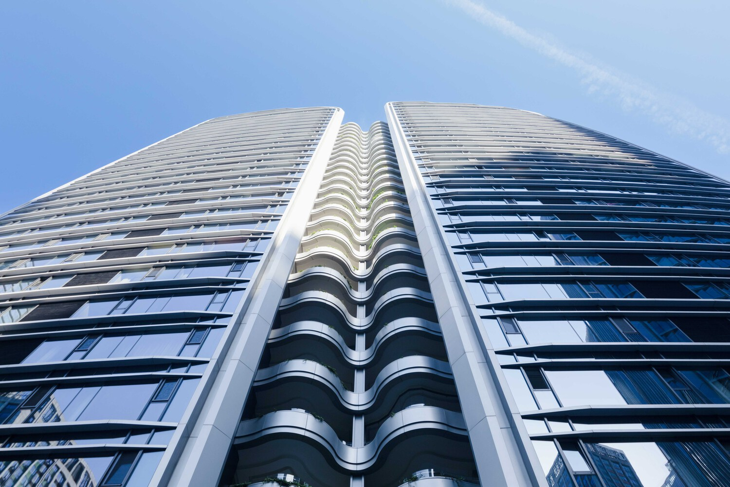 Worm's-eye view of twin glass facades meeting at central vertical spine under blue sky