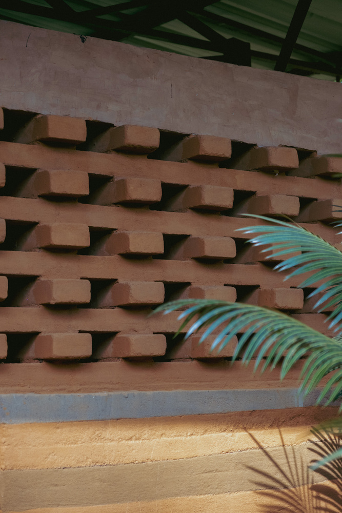 Perforated terracotta brick screen wall with palm fronds casting shadows below painted timber beams