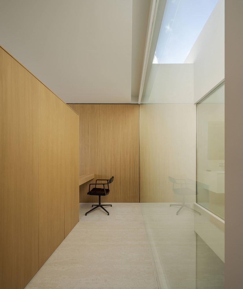 Light-filled study with vertical timber paneling and a single office chair beneath a rectangular skylight