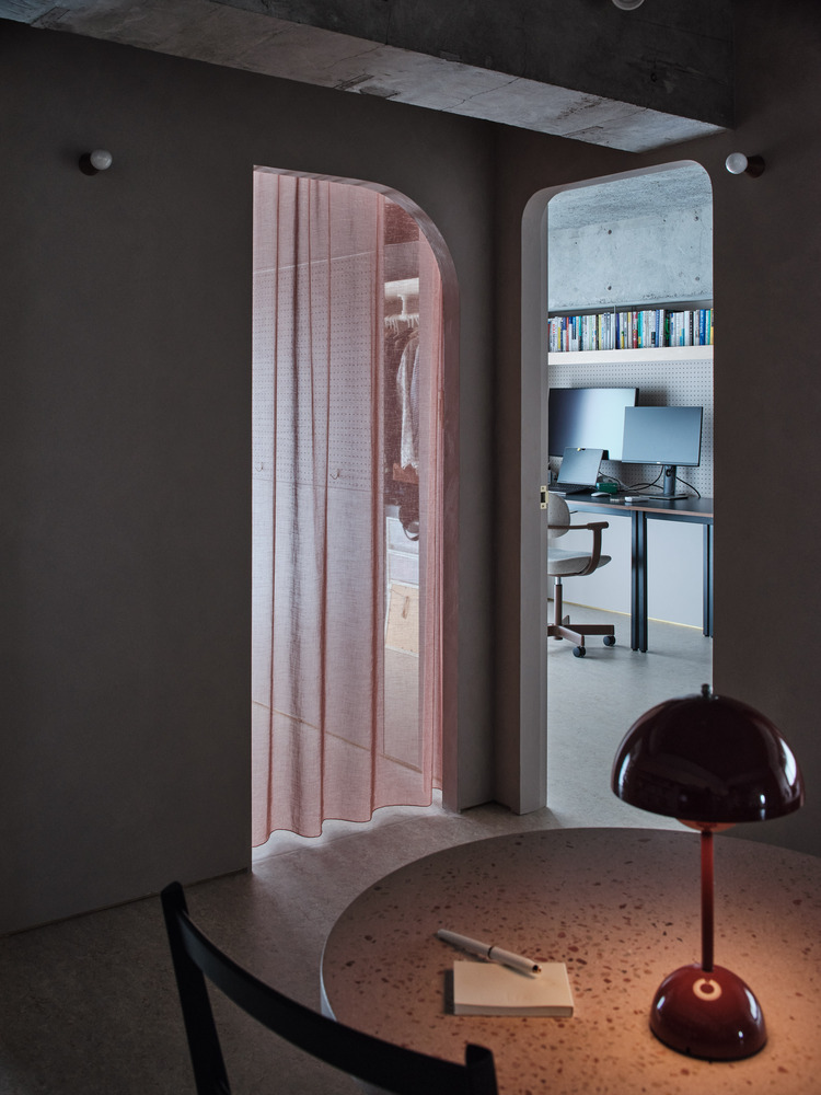 Two arched openings framing bedroom with rose curtain and office with concrete walls