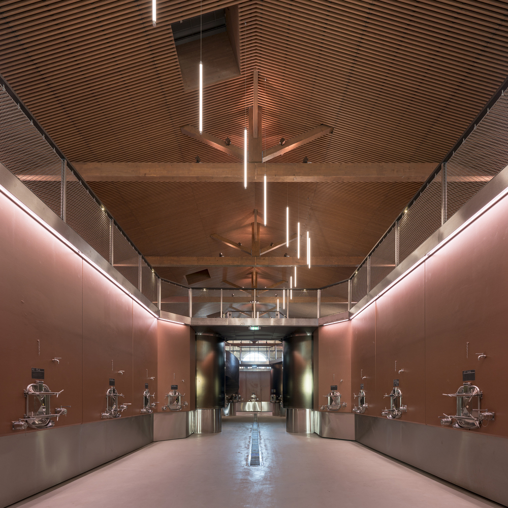 Gallery hall with timber slat ceiling, pendant linear fixtures, and bronze metal walls displaying sculptural exhibits