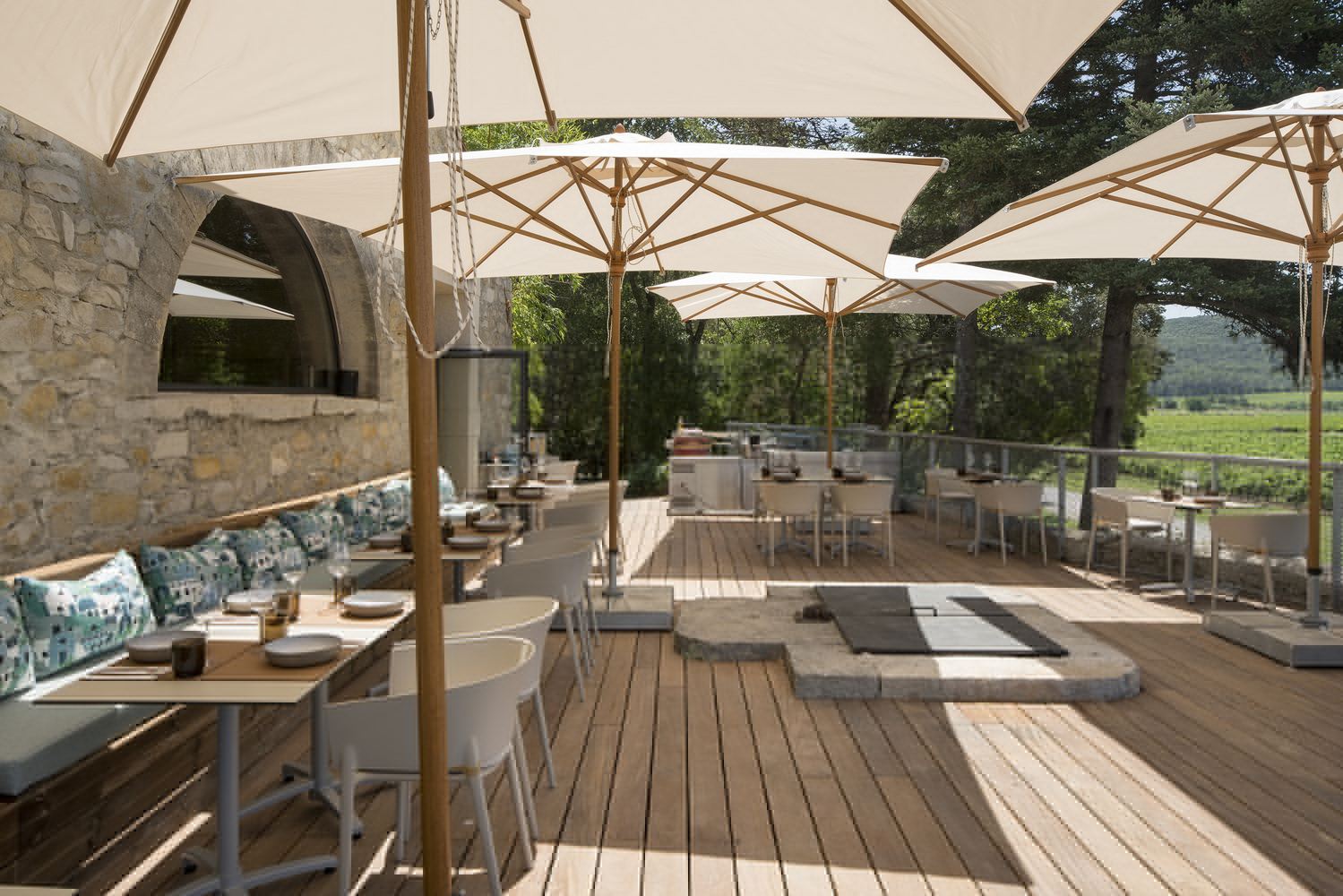 Dining terrace with timber decking, market umbrellas, stone archway, and vineyard views framed by trees