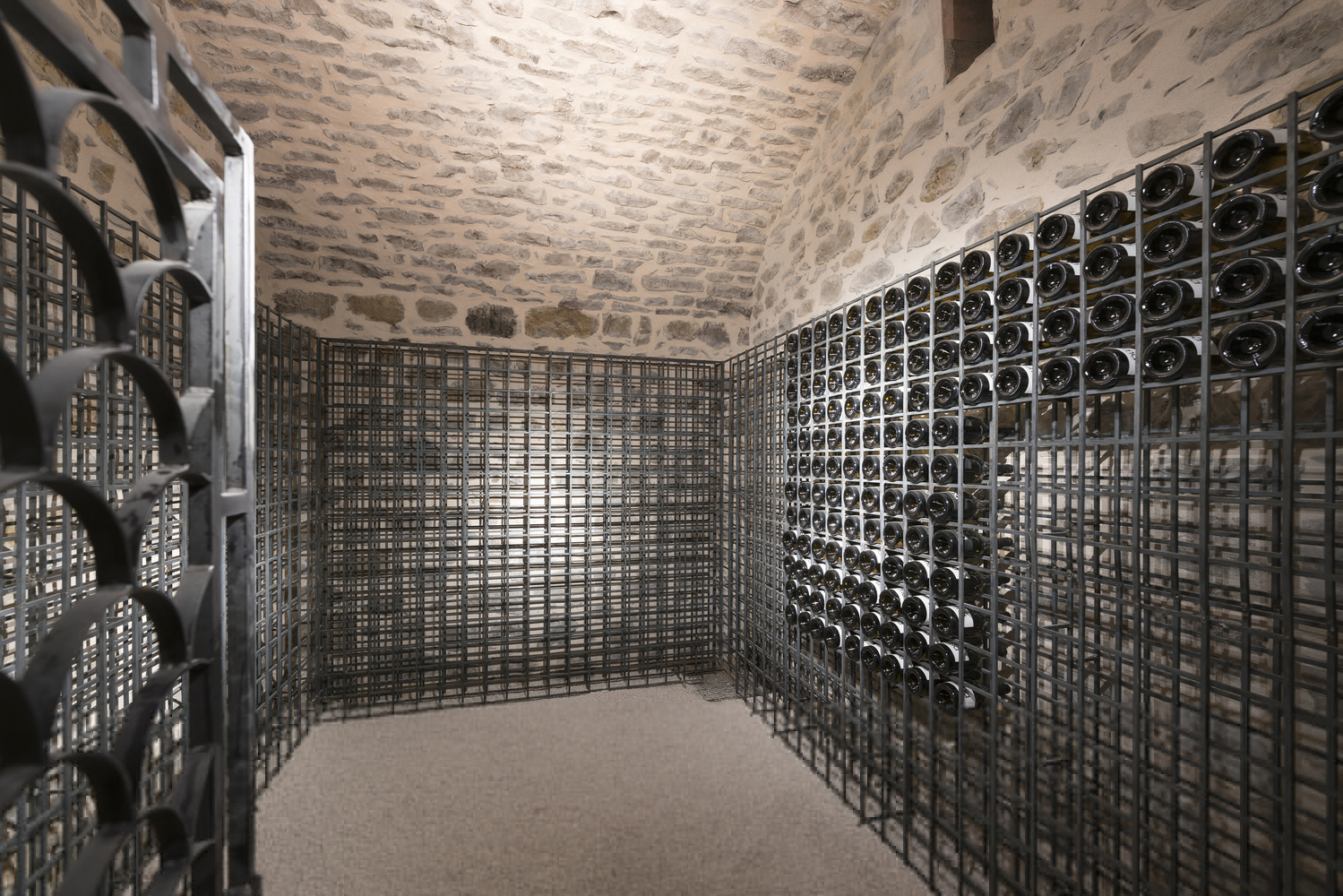 Wine cellar room with stone vaulted ceiling and floor-to-ceiling metal grid bottle racks on three walls