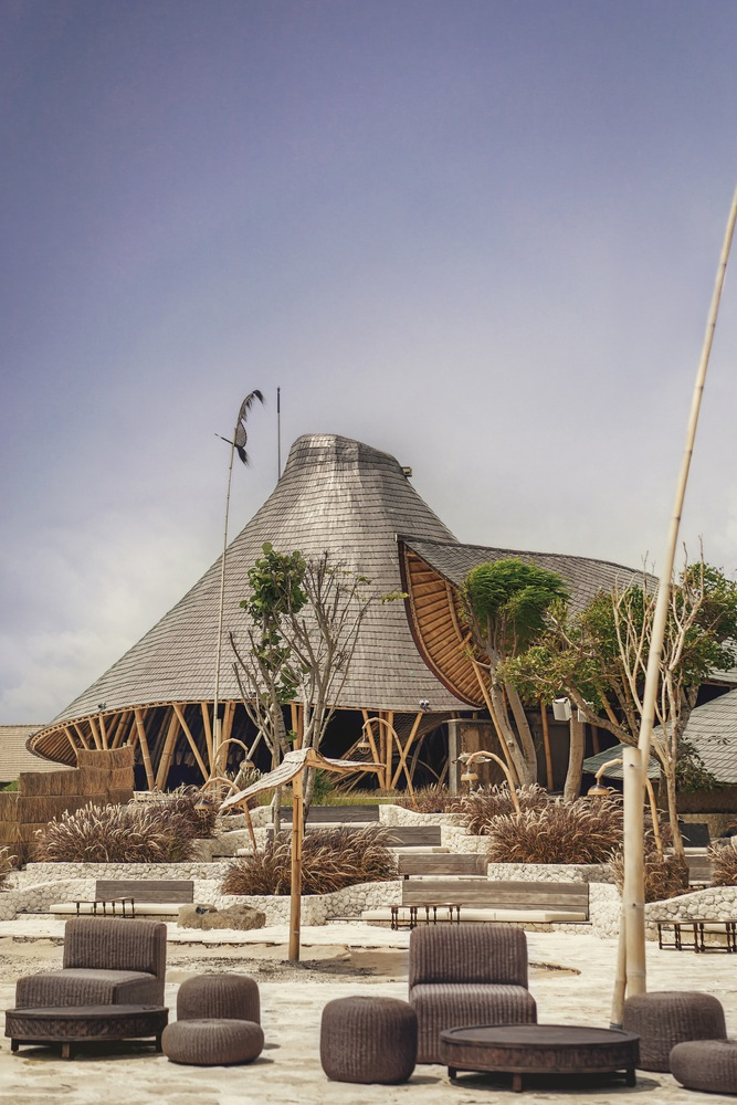 Conical shingle-clad pavilion with exposed timber columns rising above a terraced courtyard with young trees
