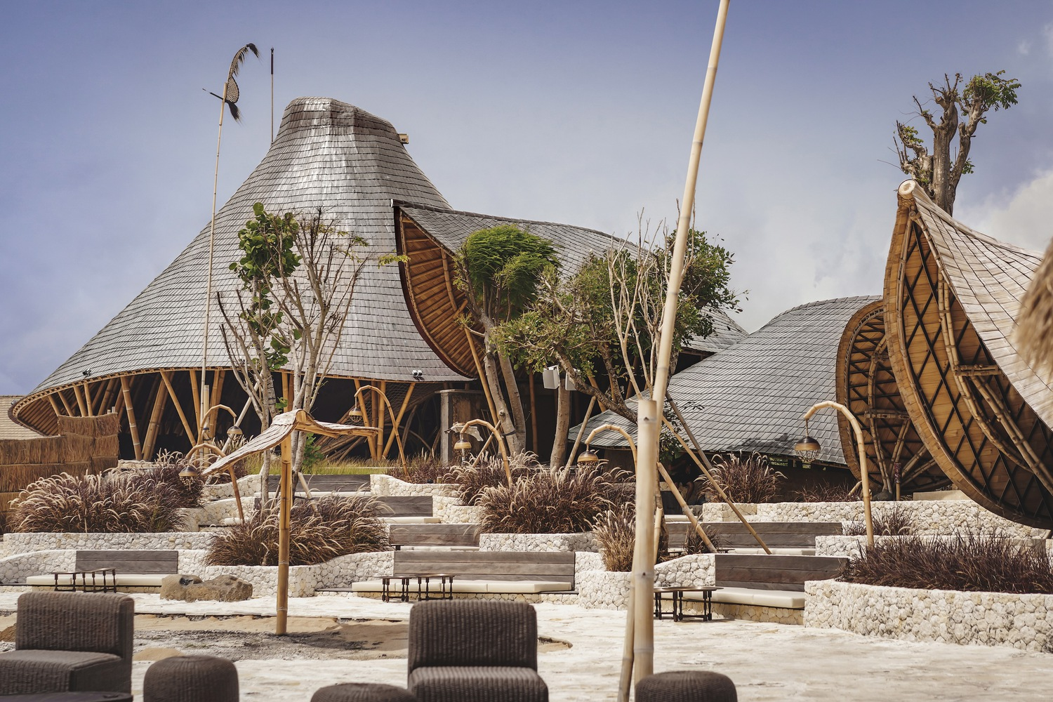 Cluster of shingle-roofed pavilions with planted terraces and woven rattan screen elements in daylight