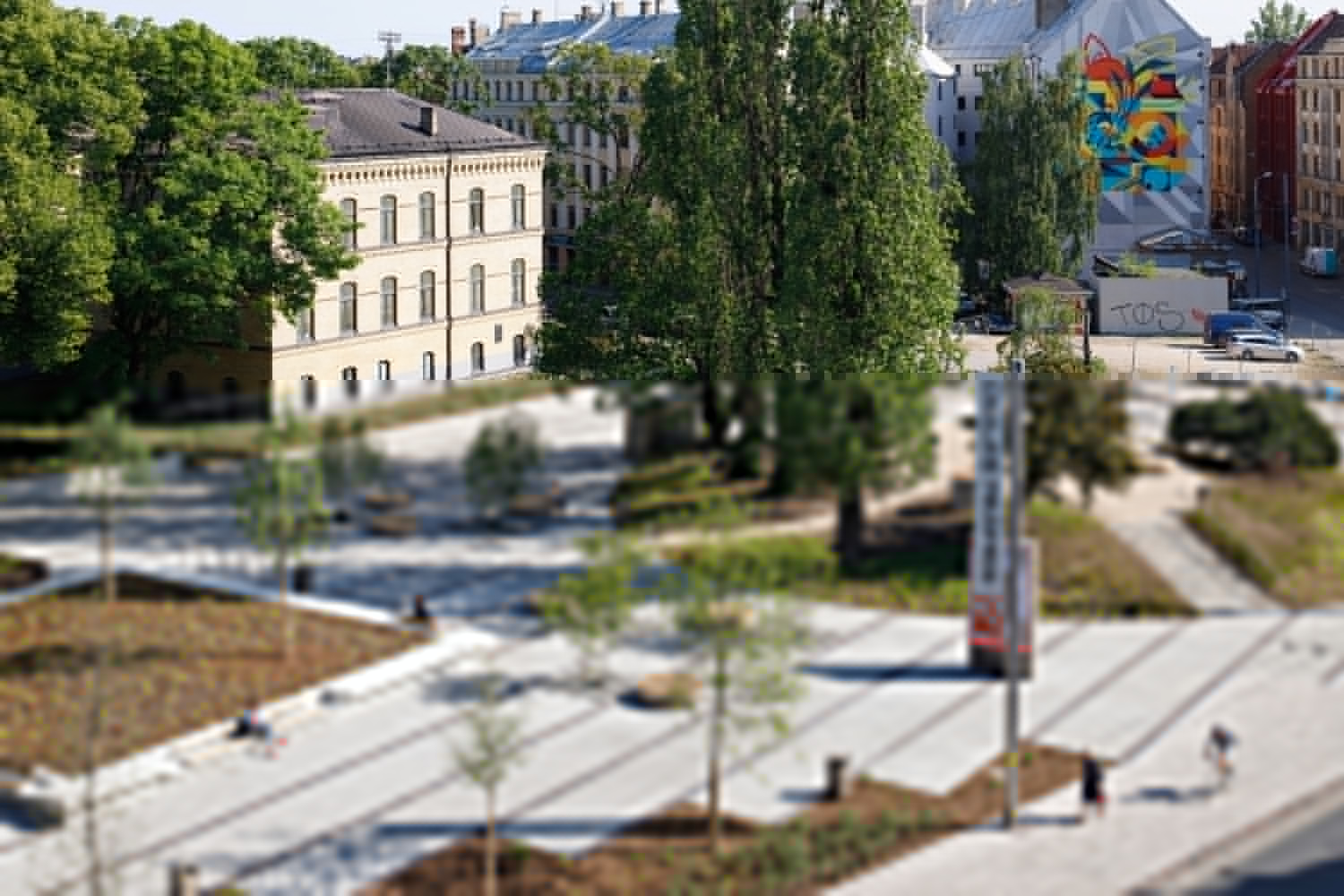 Public plaza with diagonal paving, planted beds and newly planted trees in summer sunlight