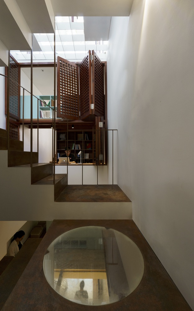 Vertical circulation space with circular floor opening and timber screened mezzanine above