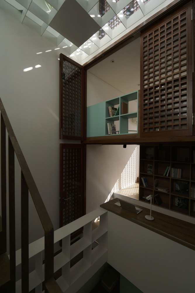 Interior courtyard with timber lattice screens and bookshelves beneath a geometric skylight casting angular shadows